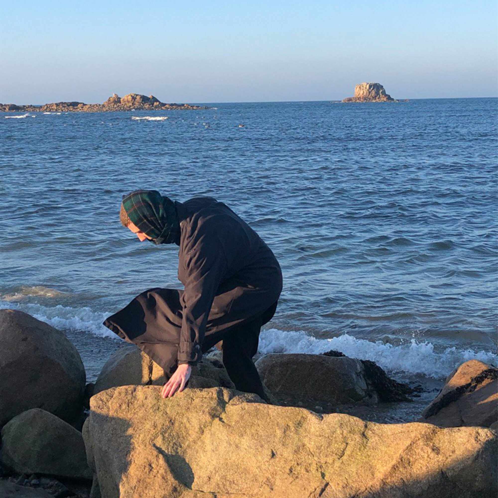 A figure, by the sea, moves across the rocks.