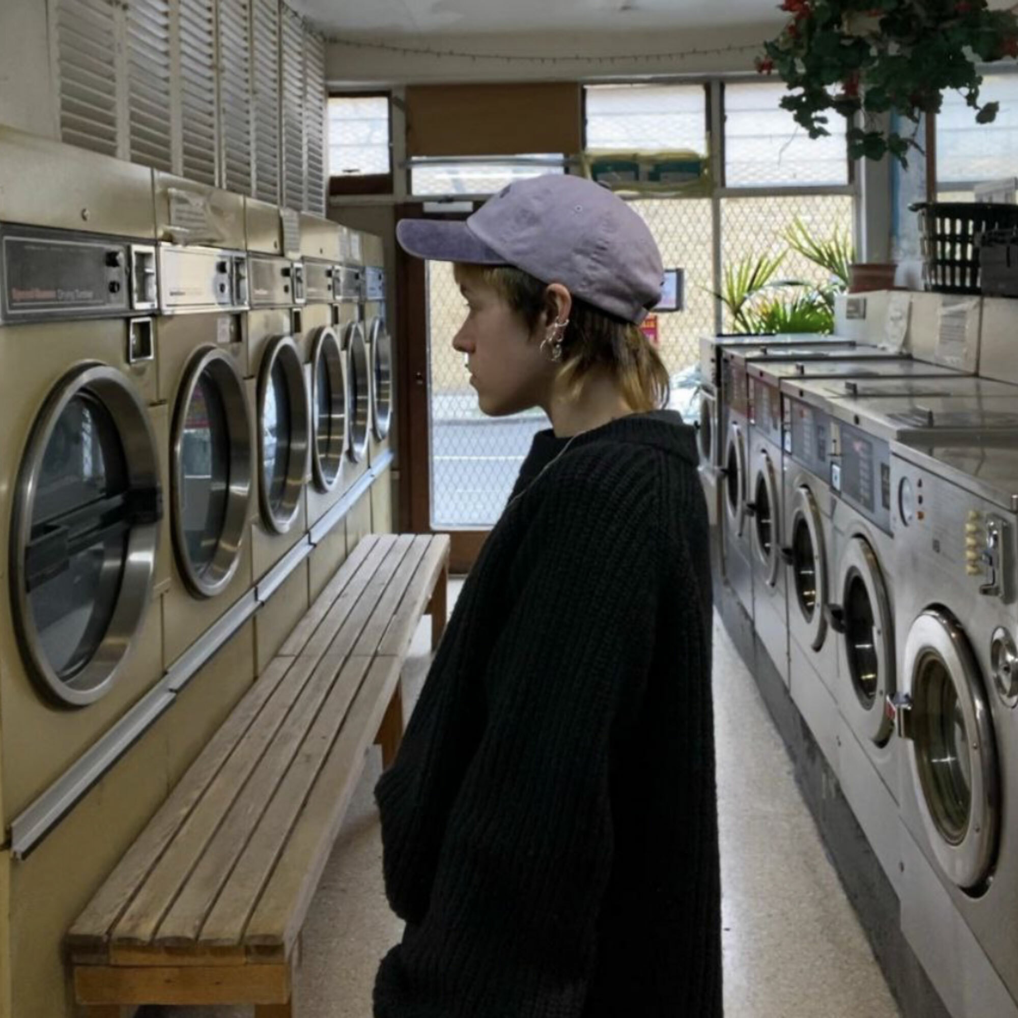 A person stands gazing at washing machines in a laundromat.